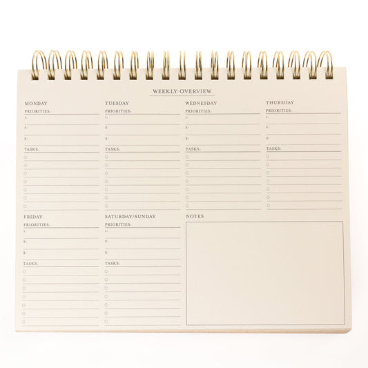 Cobalt Blue Fabric-Bound Weekly Desk Pad, A cobalt blue fabric desk pad reading days weeks in gold foil with a spiral top binding.