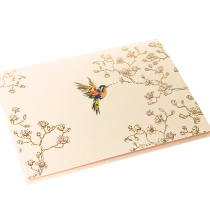 La Petite Presse Hummingbird Boxed Correspondence Notes, A cream notecard with a colorful hummingbird and gold magnolia branch line art, paired with a blush pink lined envelope.