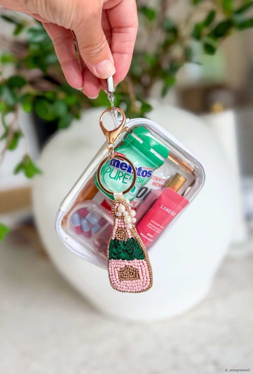Champagne Bottle Beaded Bag Charm, A hand-beaded champagne bottle bag charm in pink and gold beads with pearl bubbles, hanging from a gold key ring and lobster clasp on a printed card.