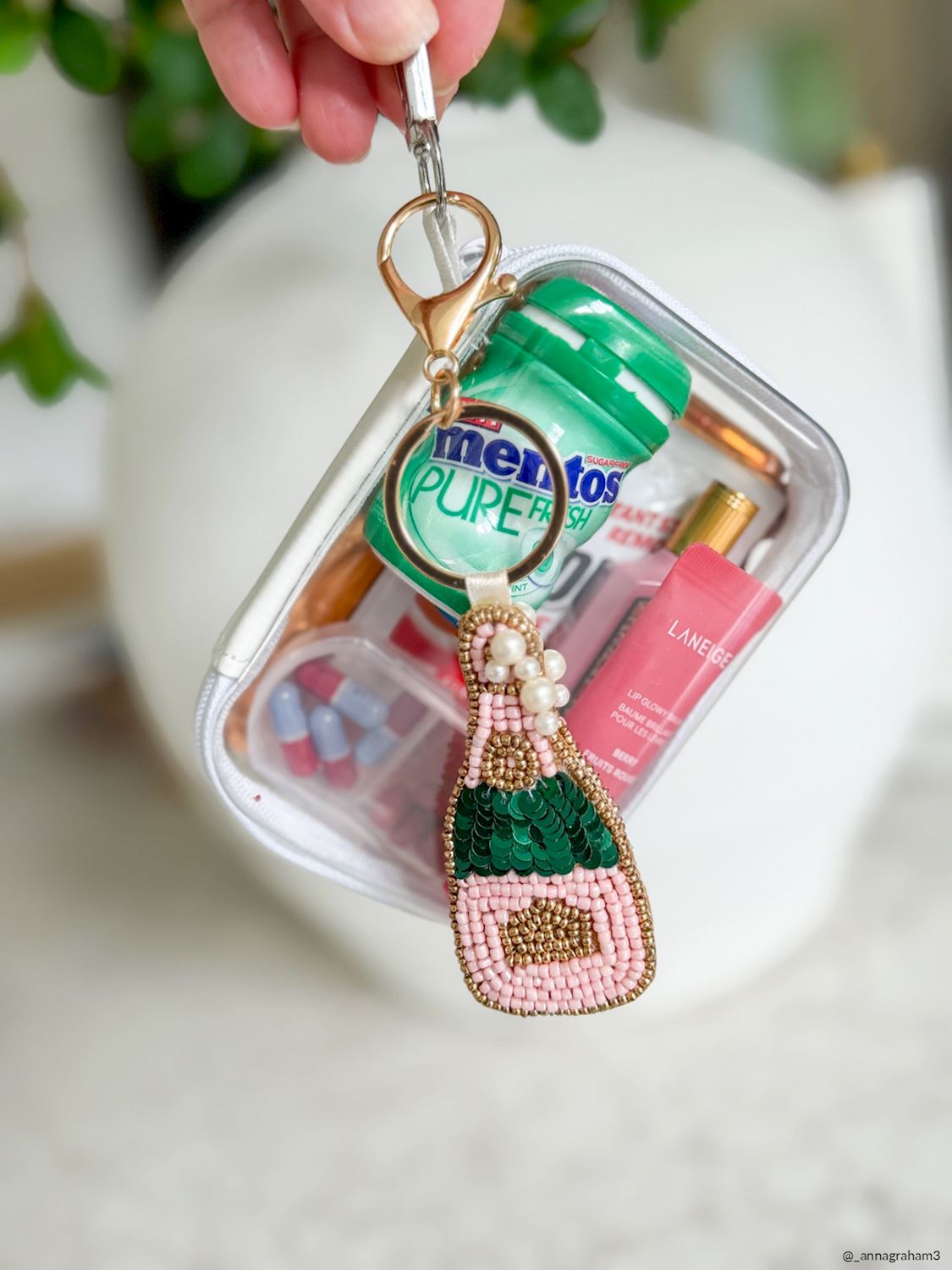 Champagne Bottle Beaded Bag Charm, A hand-beaded champagne bottle bag charm in pink and gold beads with pearl bubbles, hanging from a gold key ring and lobster clasp on a printed card.