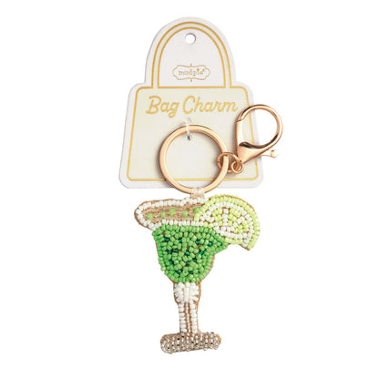 Margarita Beaded Bag Charm, A hand-beaded margarita glass charm in greens and white with a beaded lime wedge, hanging from a gold key ring and lobster clasp on a Bag Charm card.