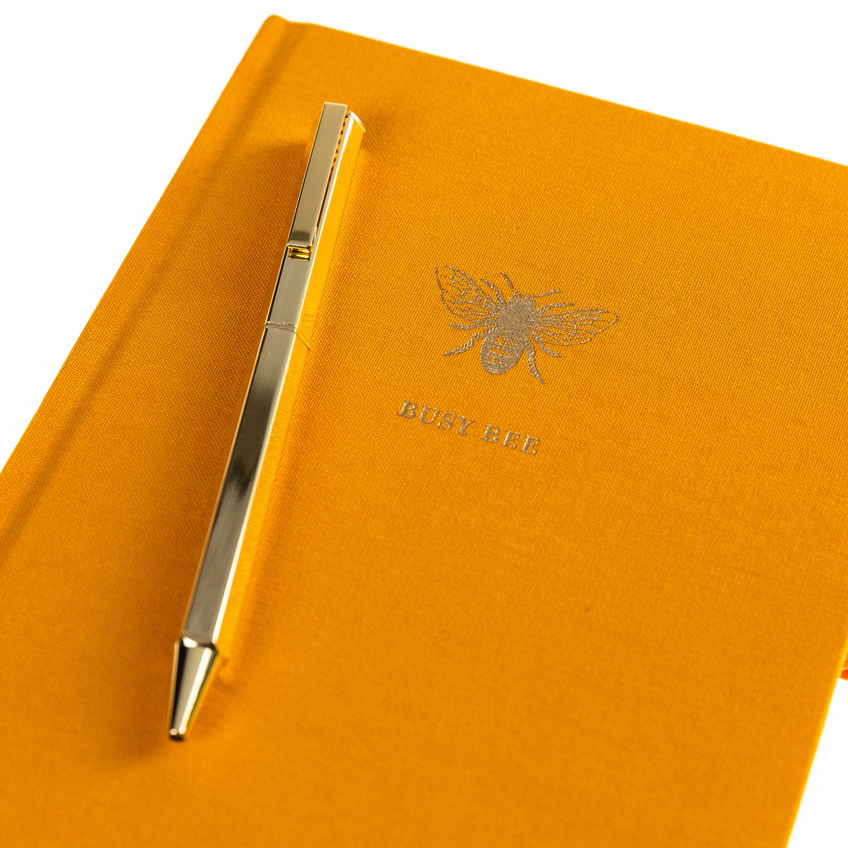 La Petite Presse Bee Fabric-Bound Journal with Pen, A marigold fabric journal with a gold foil bee and the words Busy Bee on the cover, paired with a gold twist pen.