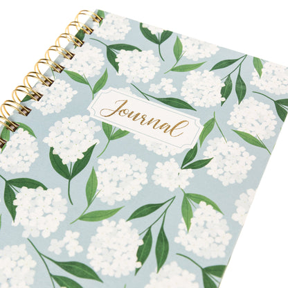 Hydrangeas Everyday Journal, A dusty blue spiral-bound journal covered in white hydrangea blooms and green leaves with a gold foil Journal label near the top.