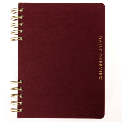Burgundy Fabric-Bound Task Journal, A burgundy fabric-covered task journal with gold twin wire spirals and two maroon ribbon bookmark tabs, closed with an elastic band.