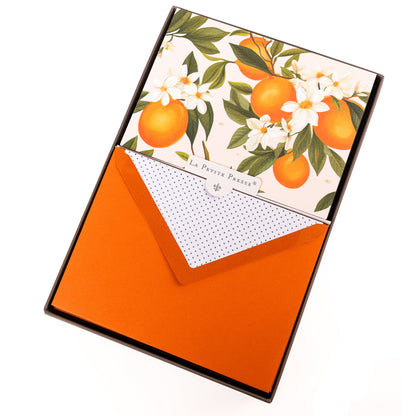 La Petite Presse L'Orange Boxed Correspondence Notes, A brown gift box open to a cream notecard printed with ripe oranges and white orange blossoms, paired with a bright orange envelope.