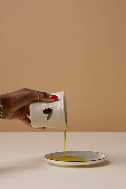 Fig & Olive Bistro Candle 8 oz, A lit ceramic candle with a hand-painted olive and leaf stands on its green Fig and Olive box.