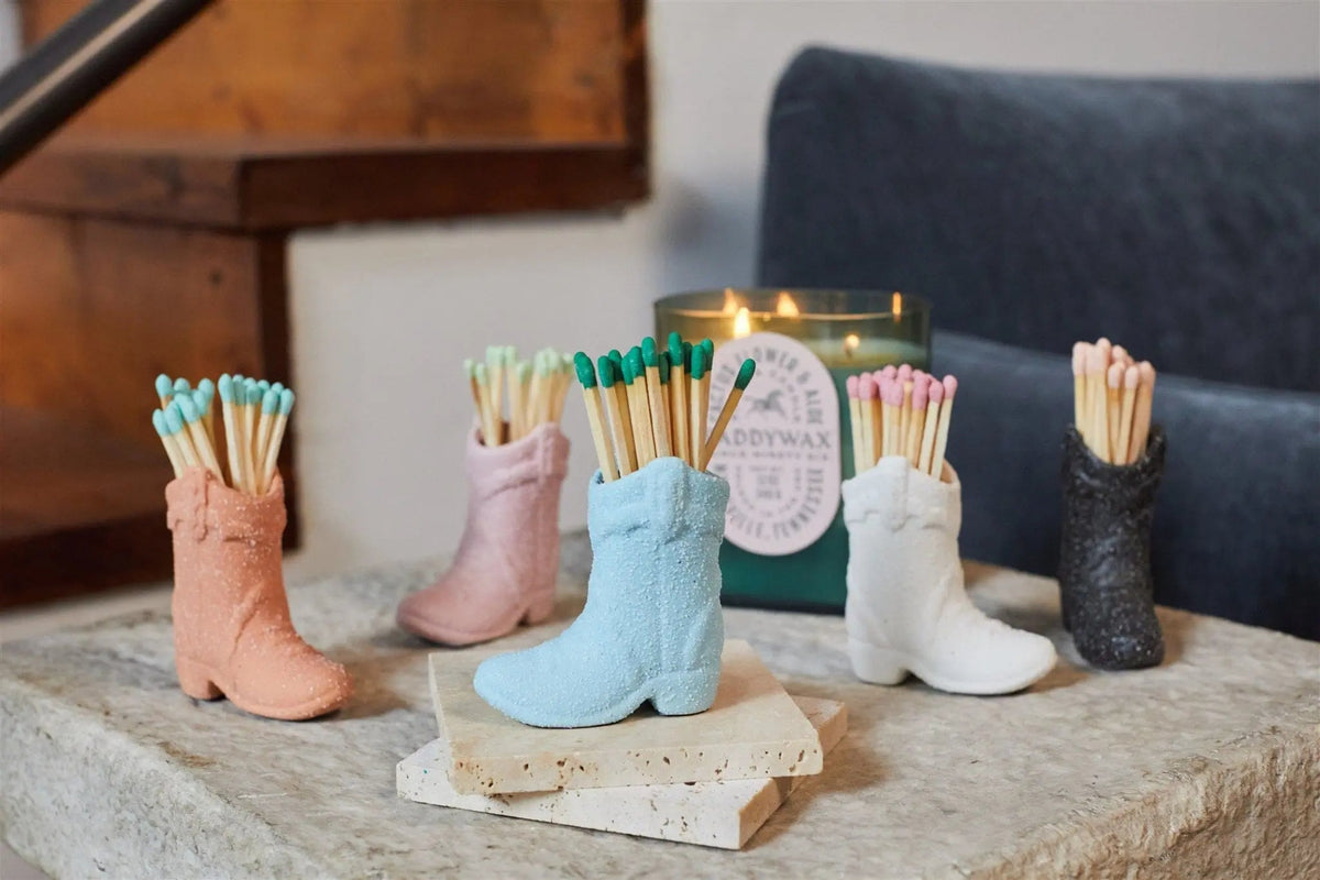 Cowboy Boot Match Holder, A matte white ceramic cowboy boot holds a bundle of pink-tipped matches beside its kraft packaging box.
