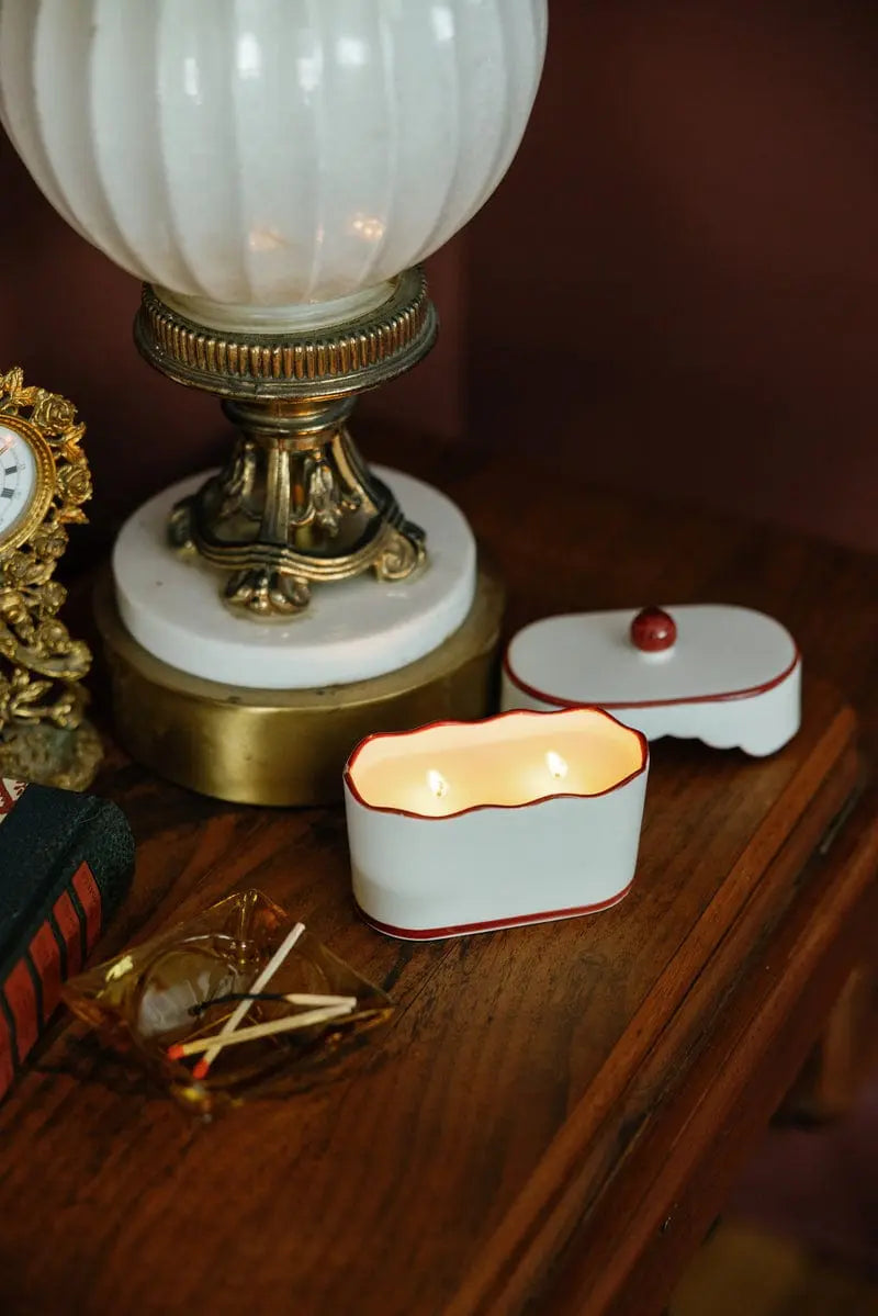 Chérie 5.5 oz Ceramic Candle, A white ceramic lidded candle box with a black scalloped rim and a round knob, tagged Black Fig and Olive.