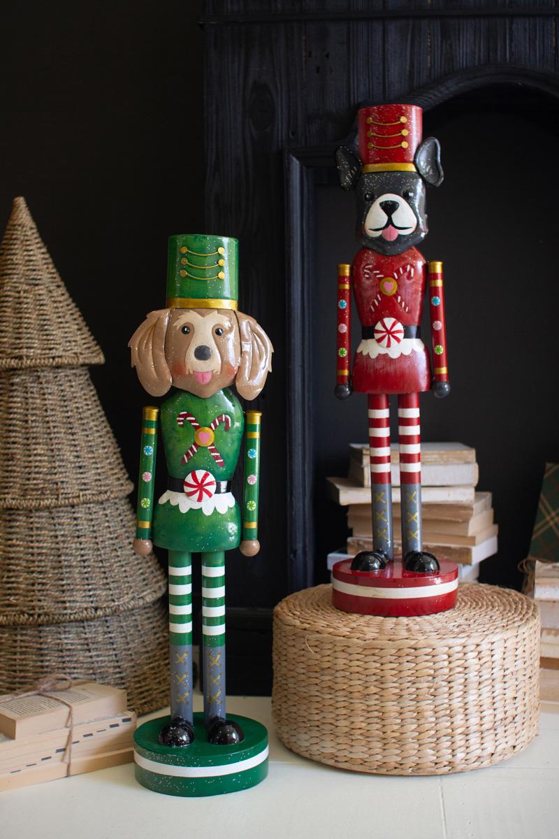 Painted Metal Dog Nutcracker, both designs standing together beside a Christmas tree, a golden retriever in a green uniform and a black and white dog in a red uniform.