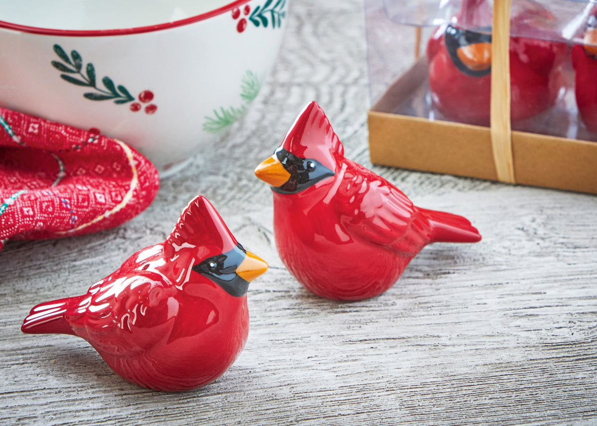 Cardinal Salt and Pepper Shakers, Two glossy red ceramic-look cardinal figurines with black masked faces and orange beaks, sitting in front of a clear box tied with a raffia bow.