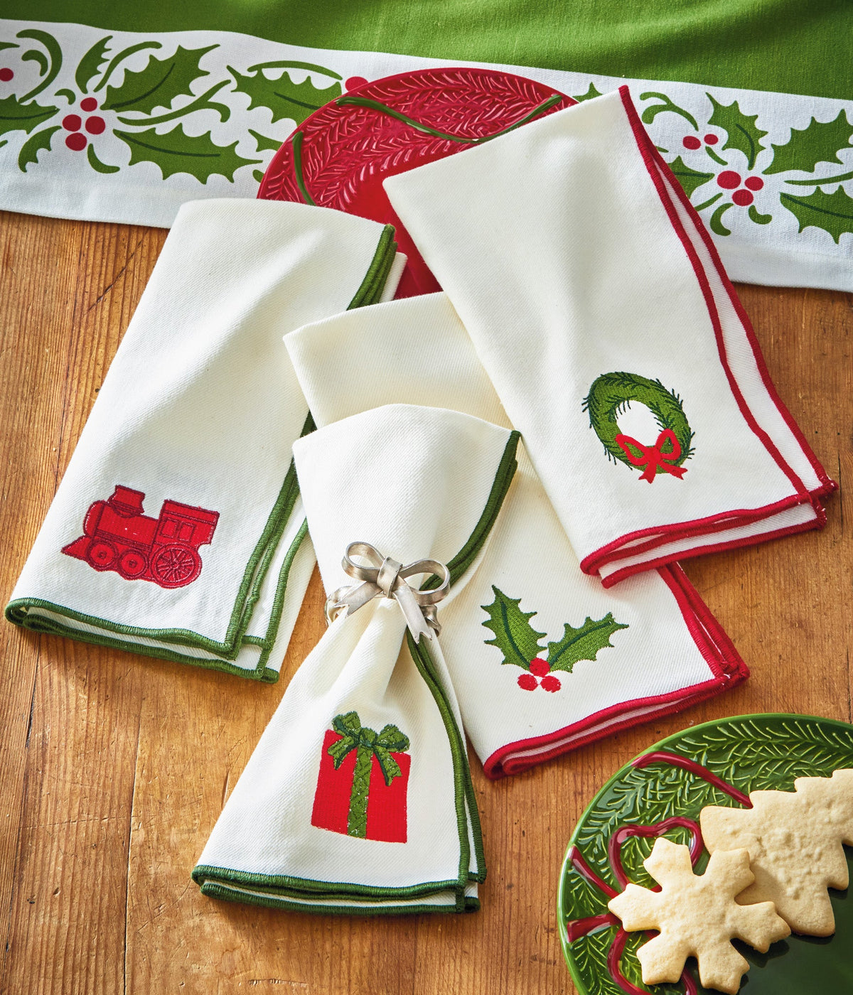 Christmastime Embroidered Napkin Set of Four, Photo shows four white napkins folded together, each embroidered with a different Christmas icon and trimmed in red or green satin.