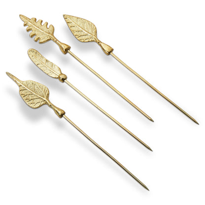 Leaf Cocktail Picks, Set of Four, Four gold metal cocktail picks with different leaf-shaped toppers, including an oak leaf and a feather shape, laid out on a white background.