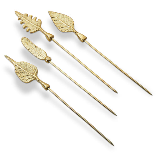 Leaf Cocktail Picks, Set of Four, Four gold metal cocktail picks with different leaf-shaped toppers, including an oak leaf and a feather shape, laid out on a white background.