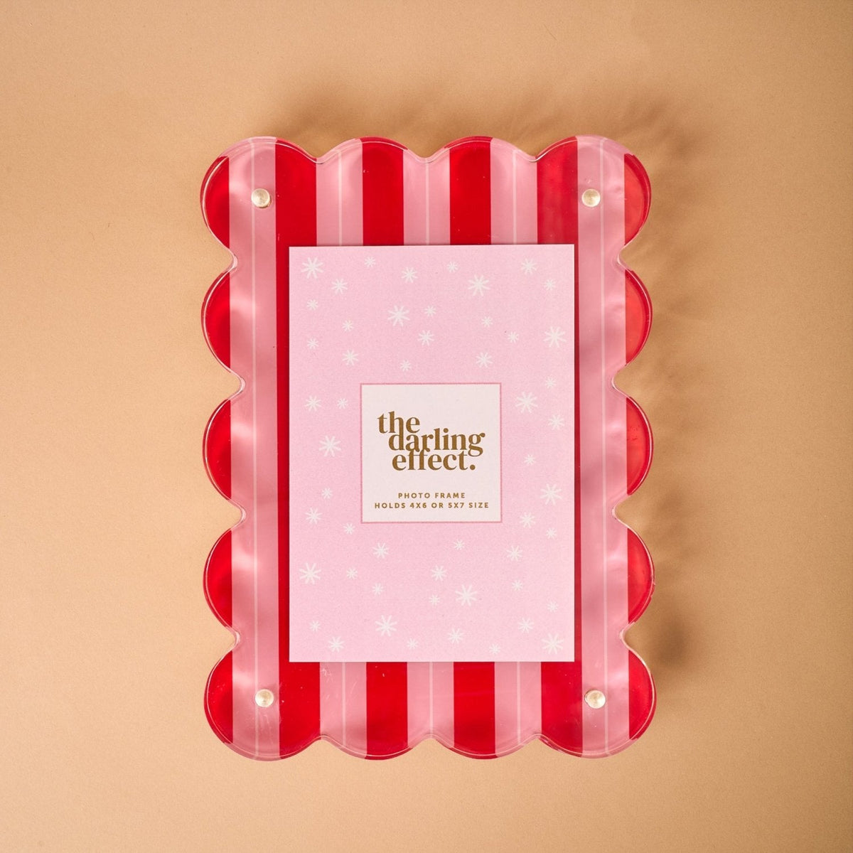 A clear acrylic picture frame with a red and pink striped, scalloped edge, holding a pink patterned insert card reading The Darling Effect Photo Frame.