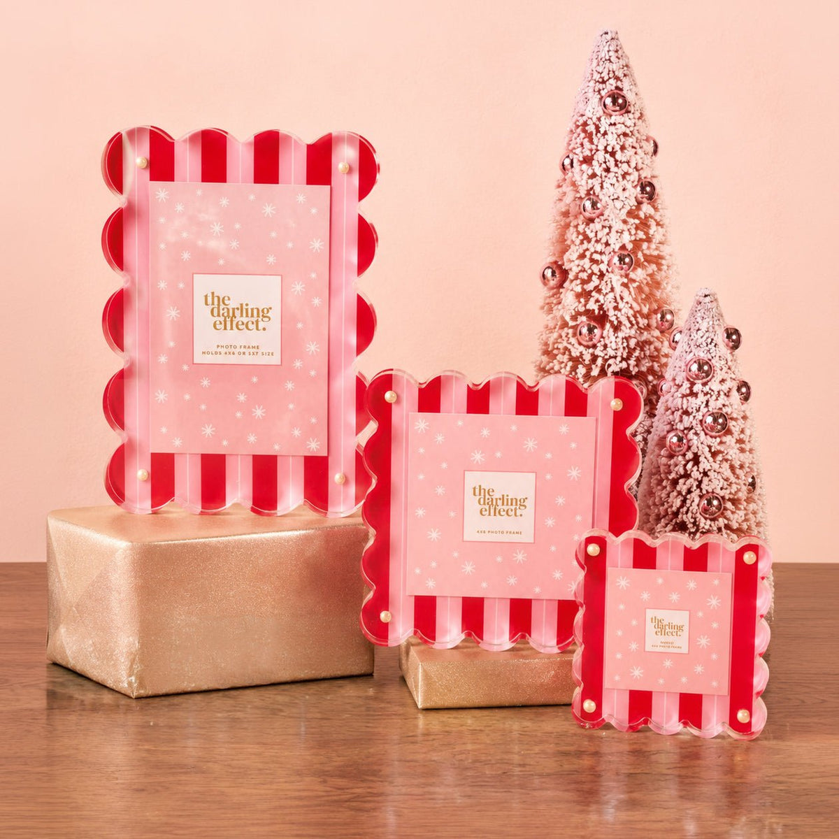 Peppermint stripes scalloped acrylic picture frames in three sizes on gold wrapped boxes beside pink bottle brush trees.