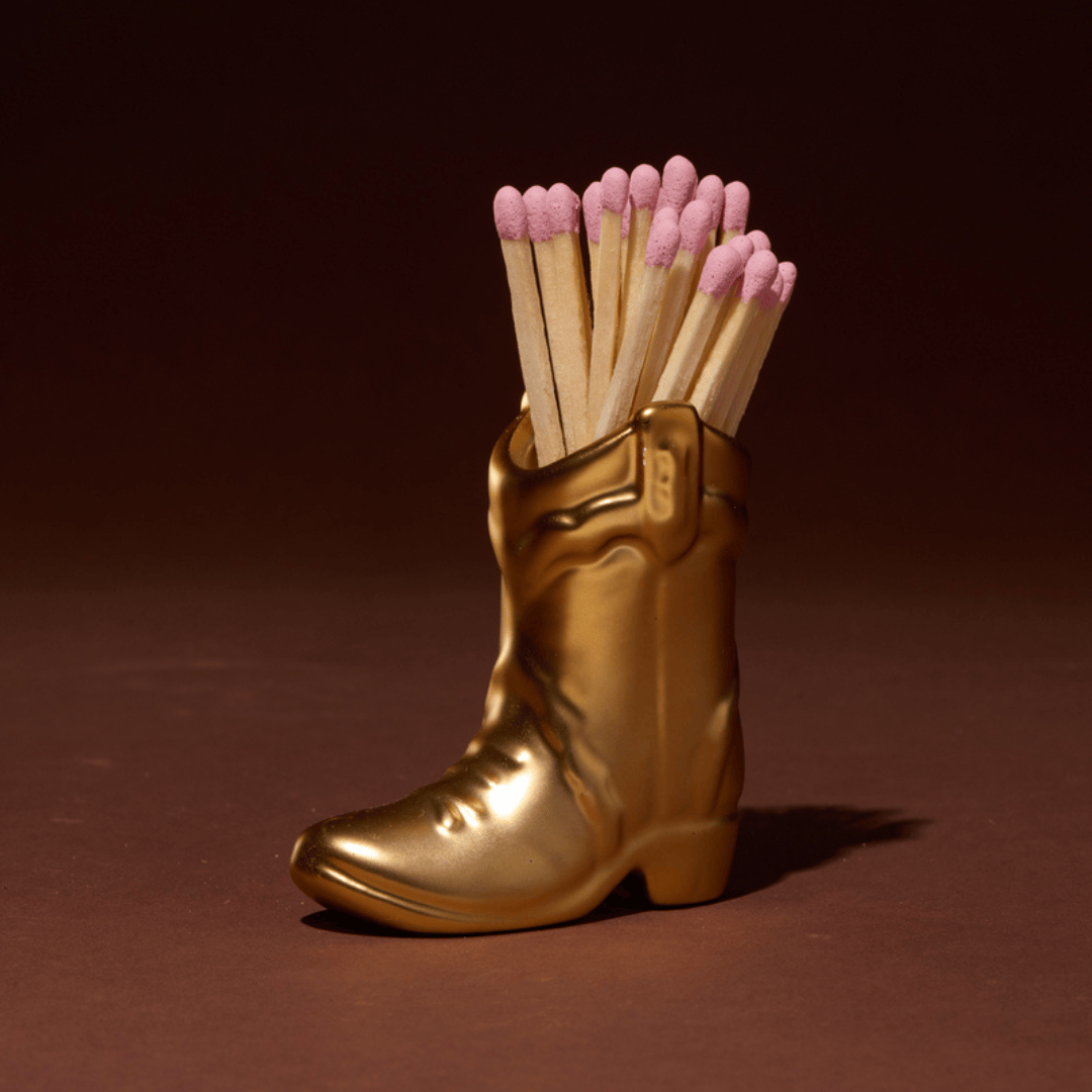 Cowboy Boot Match Holder, A matte white ceramic cowboy boot holds a bundle of pink-tipped matches beside its kraft packaging box.