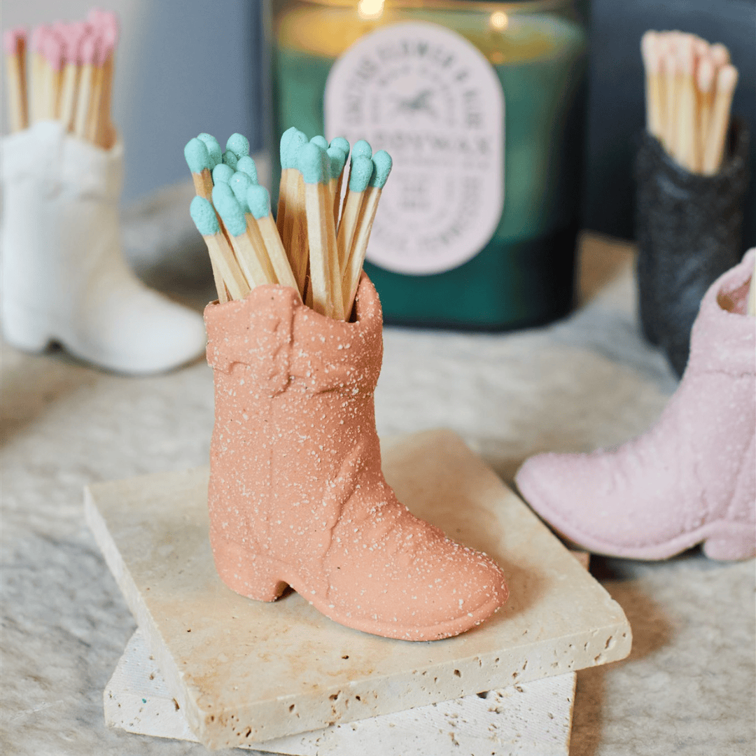 Cowboy Boot Match Holder, A matte white ceramic cowboy boot holds a bundle of pink-tipped matches beside its kraft packaging box.