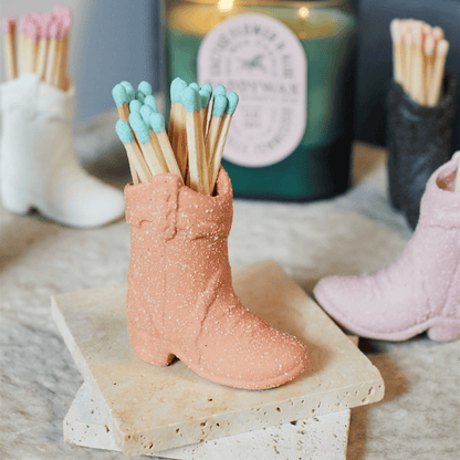 Cowboy Boot Match Holder, A matte white ceramic cowboy boot holds a bundle of pink-tipped matches beside its kraft packaging box.