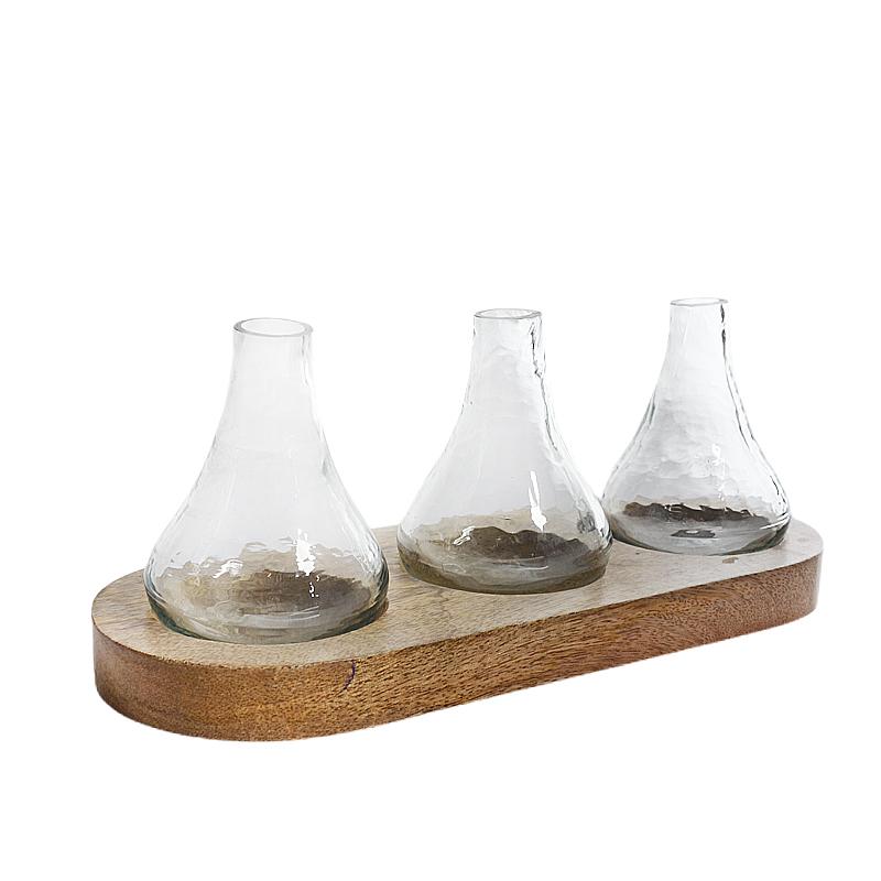 Dahlia Glass Bud Vase with Wooden Tray, Three clear glass bud vases, each a different shape, set on an oval mango wood tray against a white background.