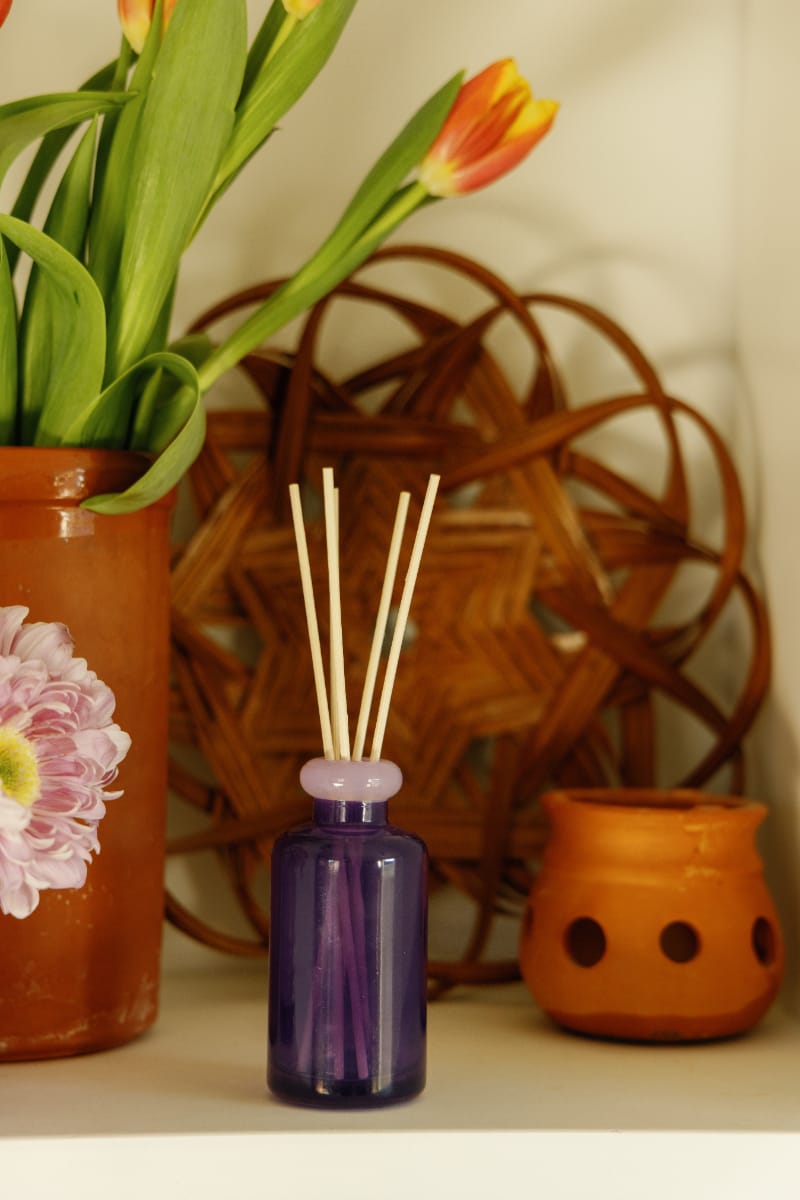 Stack 3.2 oz Diffuser, A maroon glass reed diffuser bottle with pink topped reeds standing next to its packaging box labeled Saffron Rose.