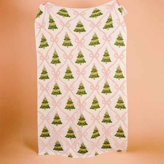Twinkling Trees Cozy Dreams Luxe Blanket, A cream throw blanket printed with a pattern of green Christmas trees connected by a pink ribbon lattice, held up to show the full design.