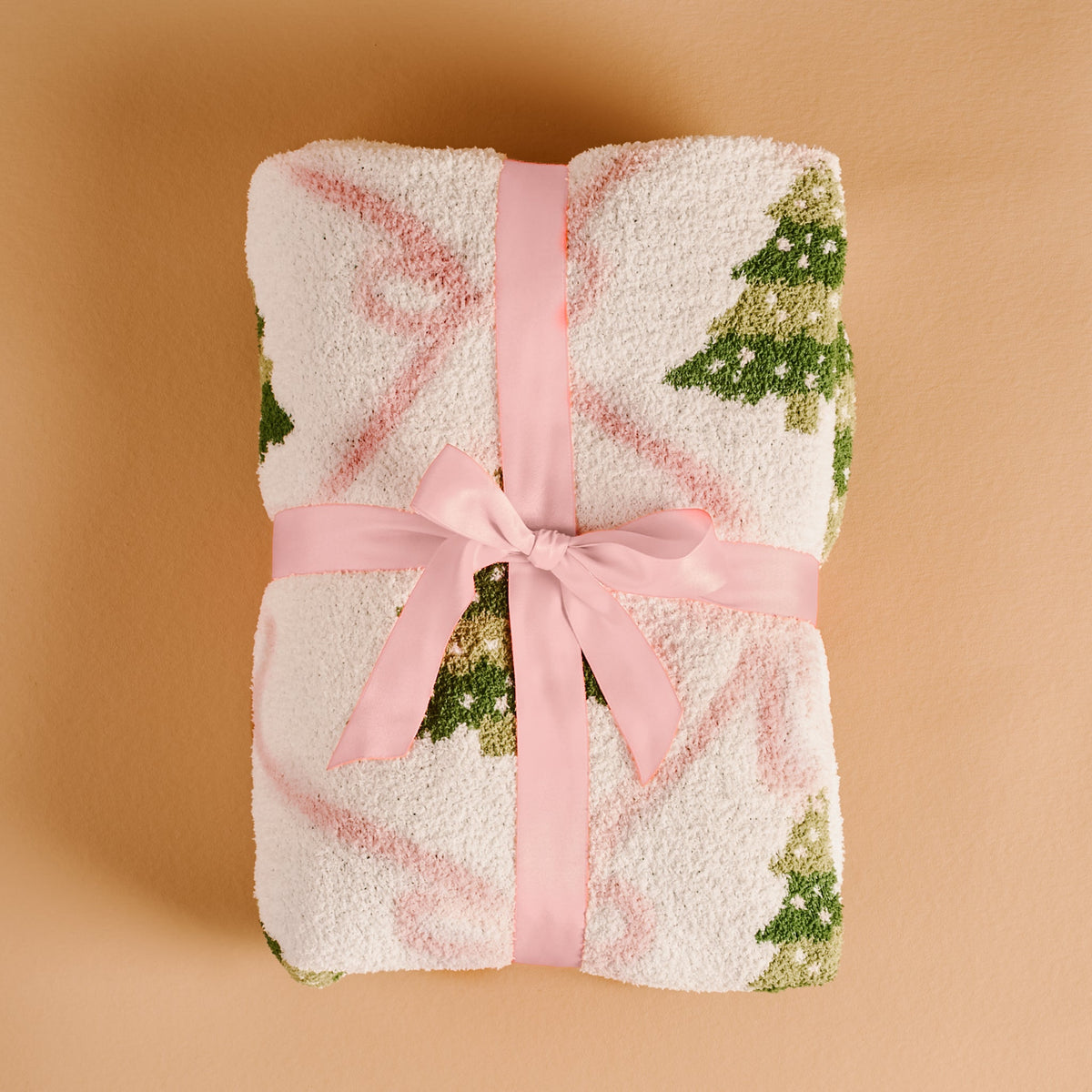 Twinkling Trees Cozy Dreams Luxe Blanket, A cream throw blanket printed with a pattern of green Christmas trees connected by a pink ribbon lattice, held up to show the full design.
