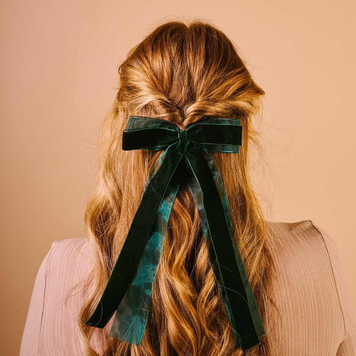 Velvet Luxe Layered Hair Bow, A deep green velvet bow with long tails and a sheer edge, laid flat against a pink background.