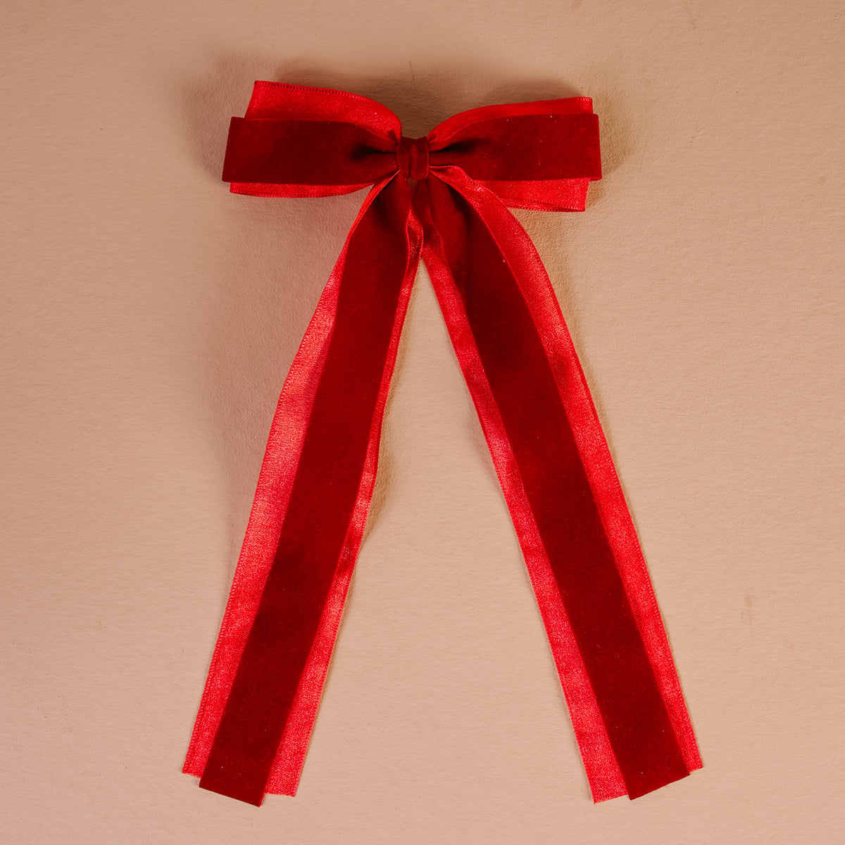 Velvet Luxe Layered Hair Bow, A deep green velvet bow with long tails and a sheer edge, laid flat against a pink background.
