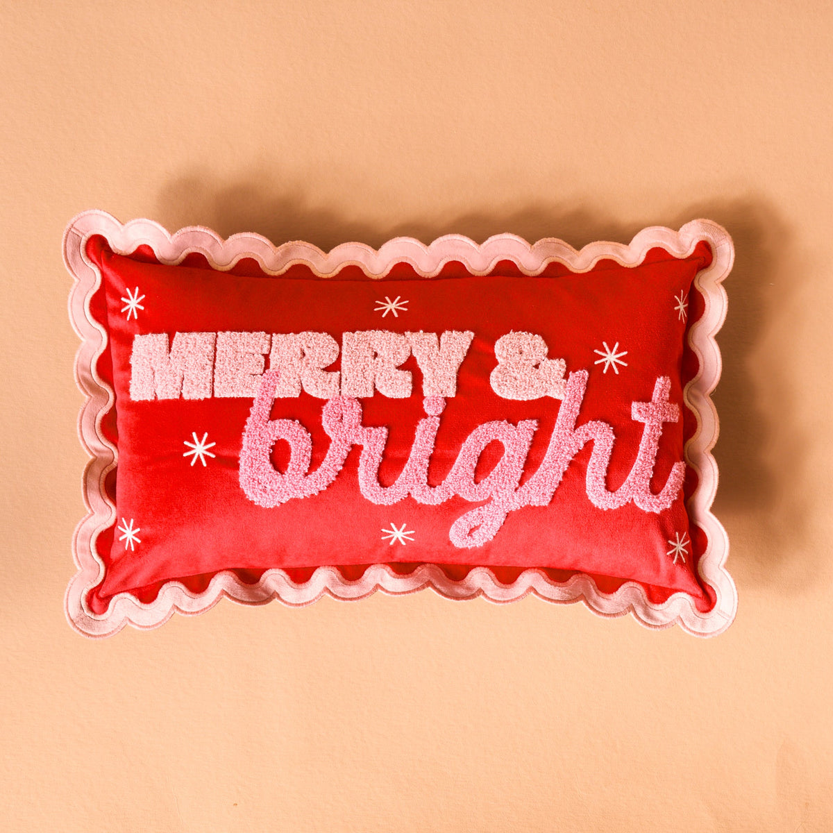 Scalloped Rectangle Throw Pillow, A blush pink lumbar pillow with three tufted green Christmas trees tied in red bows and a pink scalloped edge, set on a boucle chair.