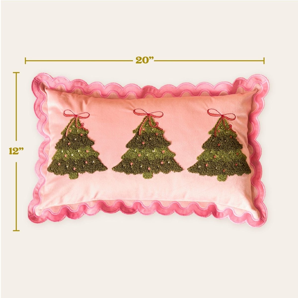 Scalloped Rectangle Throw Pillow, A blush pink lumbar pillow with three tufted green Christmas trees tied in red bows and a pink scalloped edge, set on a boucle chair.