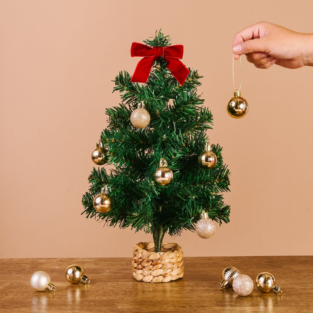 Green Mini Artificial Christmas Tree, A small artificial Christmas tree with full green branches, a red velvet bow at the top, and a woven basket base.