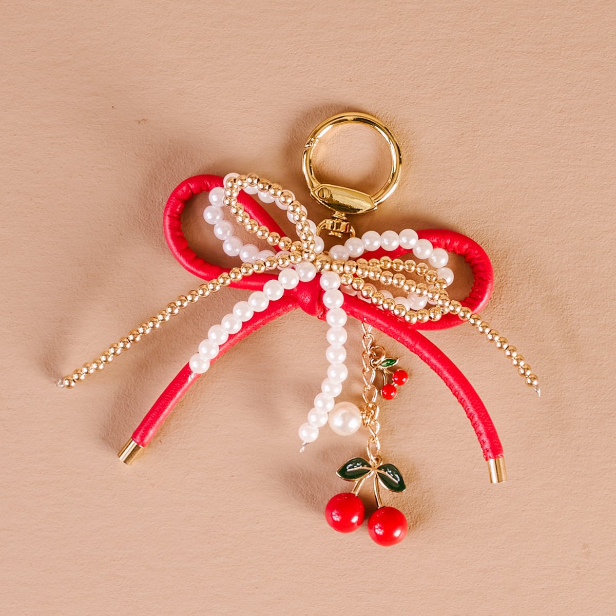 Layered Bows Bag Charm, A black bow bag charm strung with pearl and gold beads and finished with a small black flower and heart charm, clipped to a gold keyring.