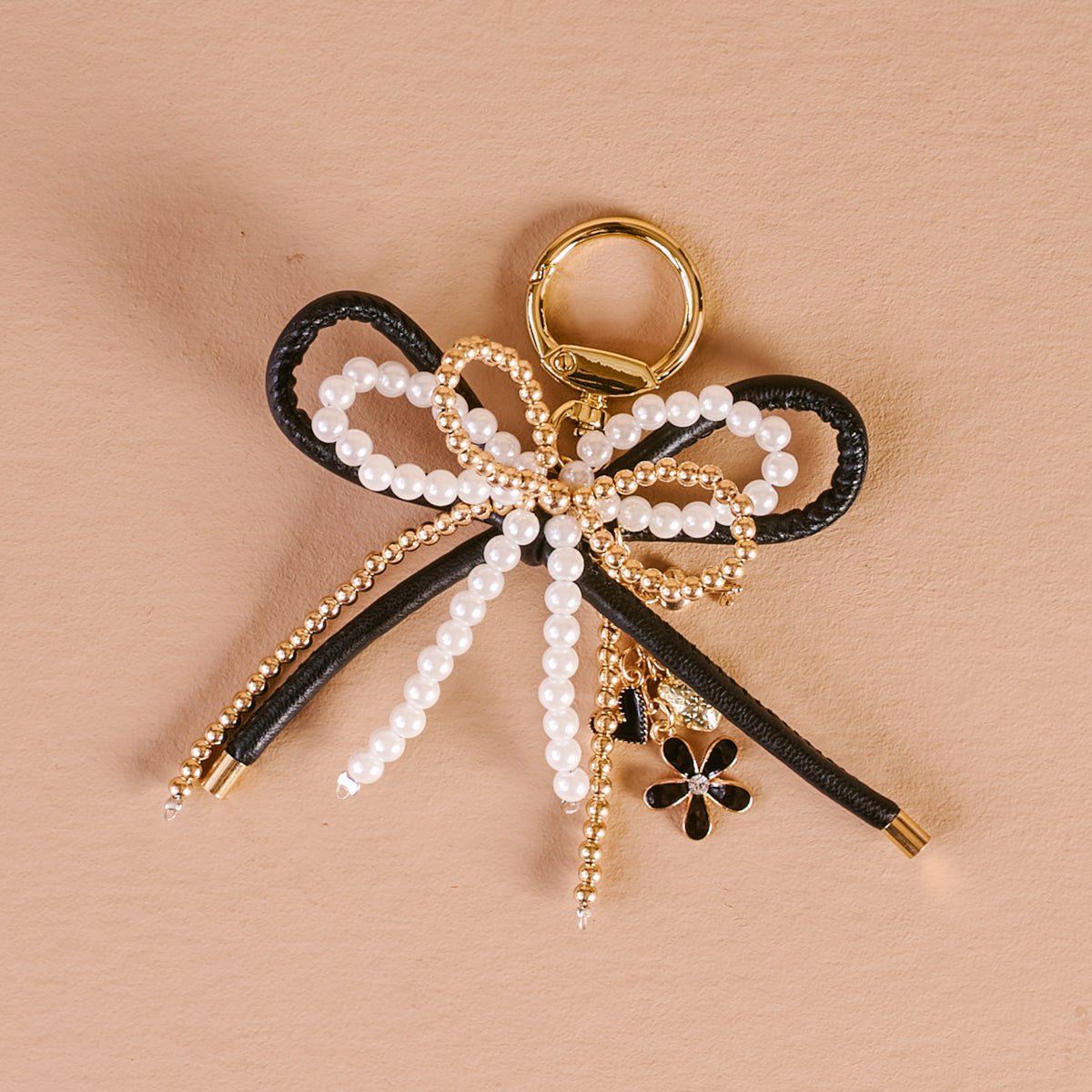 Layered Bows Bag Charm, A black bow bag charm strung with pearl and gold beads and finished with a small black flower and heart charm, clipped to a gold keyring.