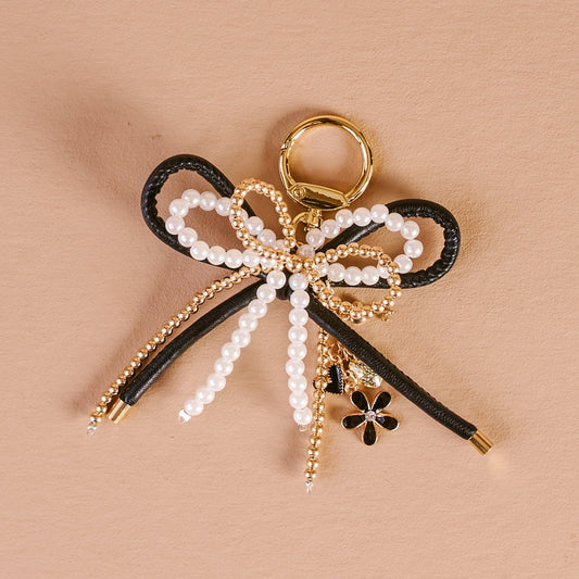 Layered Bows Bag Charm, A black bow bag charm strung with pearl and gold beads and finished with a small black flower and heart charm, clipped to a gold keyring.