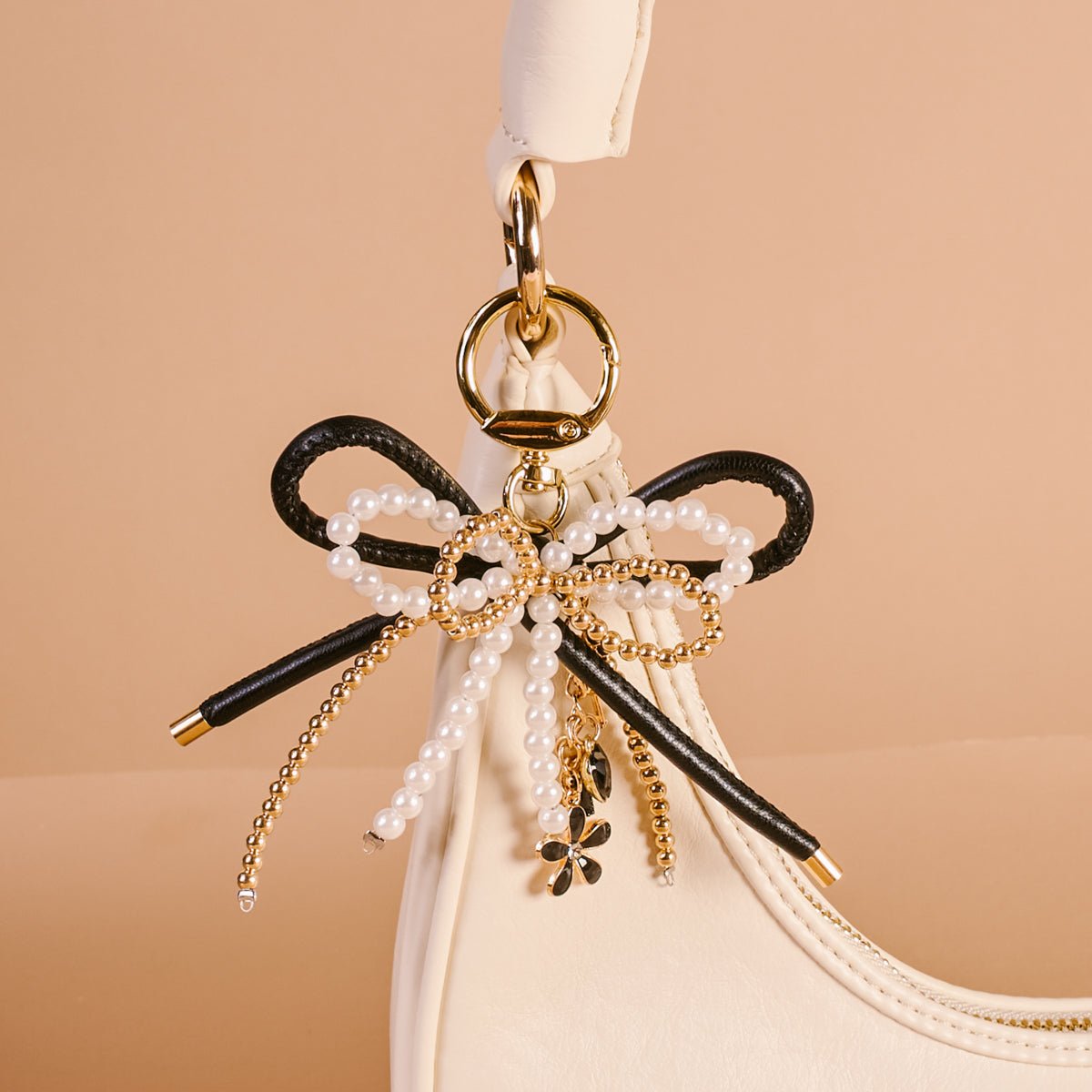 Layered Bows Bag Charm, A black bow bag charm strung with pearl and gold beads and finished with a small black flower and heart charm, clipped to a gold keyring.