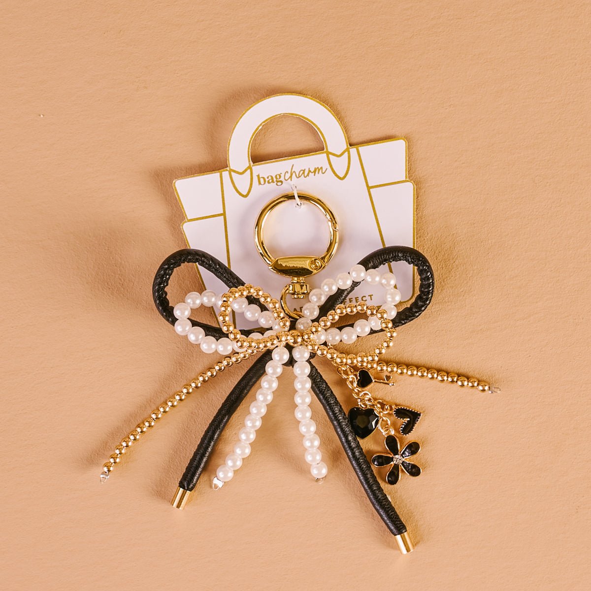 Layered Bows Bag Charm, A black bow bag charm strung with pearl and gold beads and finished with a small black flower and heart charm, clipped to a gold keyring.