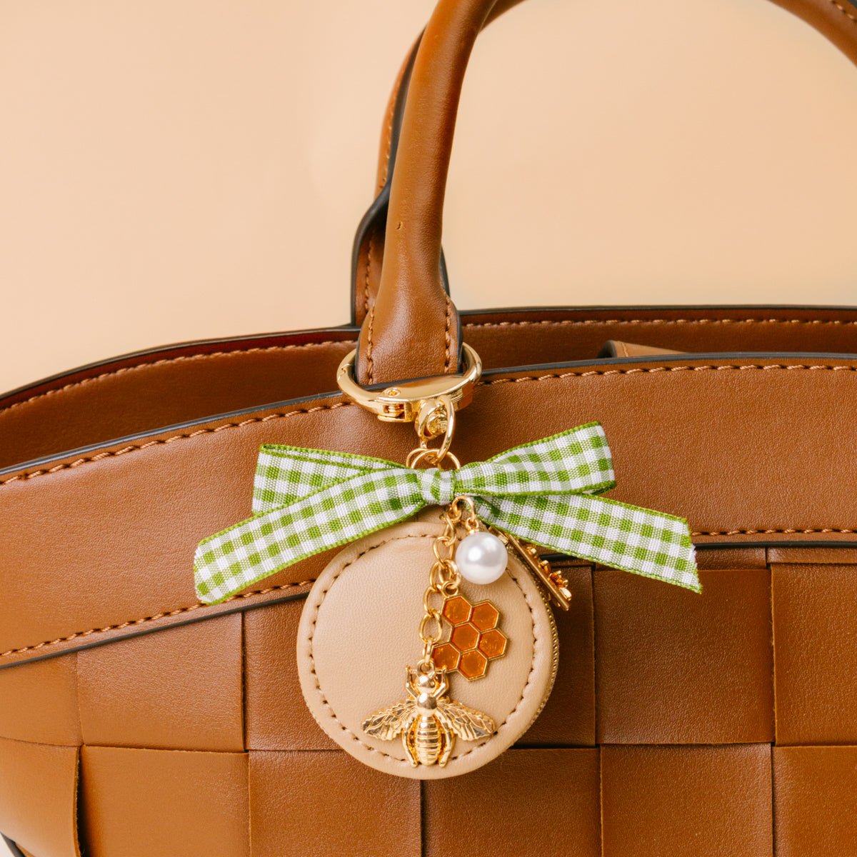 Travel Jewelry Case Bag Charm, A tan round zip case charm with a green gingham bow, a pearl, a gold bee, and a honeycomb charm, in the Hey Honey design.