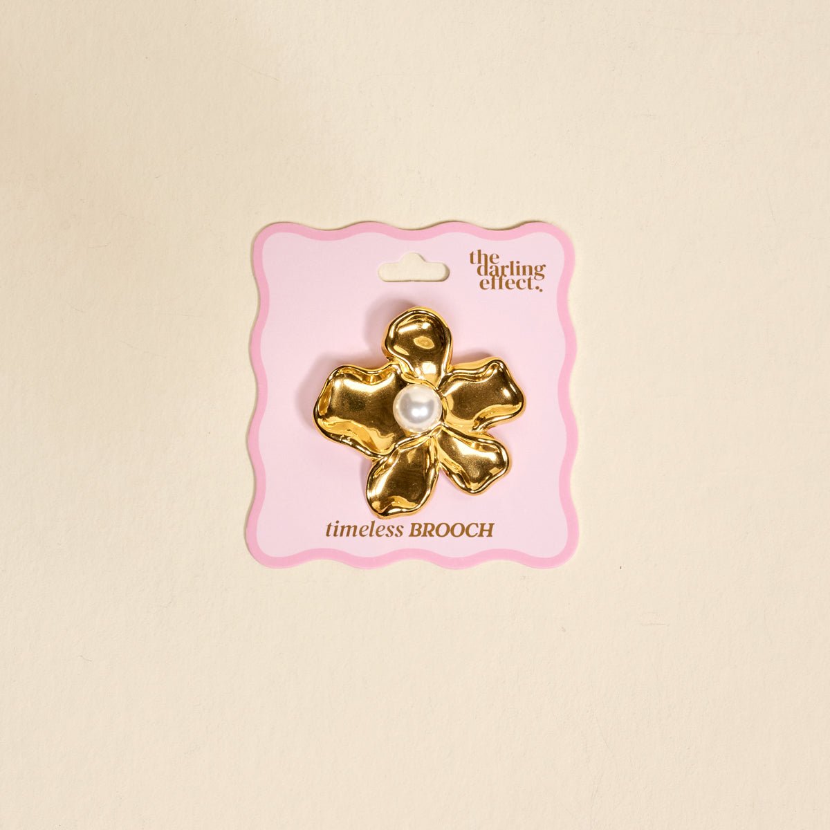 Timeless Brooch, A small gold brooch pin shaped like a teddy bear and covered edge to edge in clear rhinestones, with a gold bow at its neck, shown on a tan background.