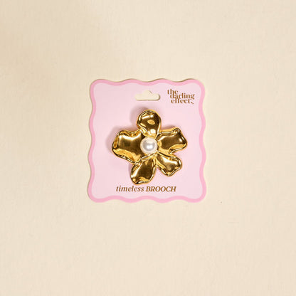 Timeless Brooch, A small gold brooch pin shaped like a teddy bear and covered edge to edge in clear rhinestones, with a gold bow at its neck, shown on a tan background.