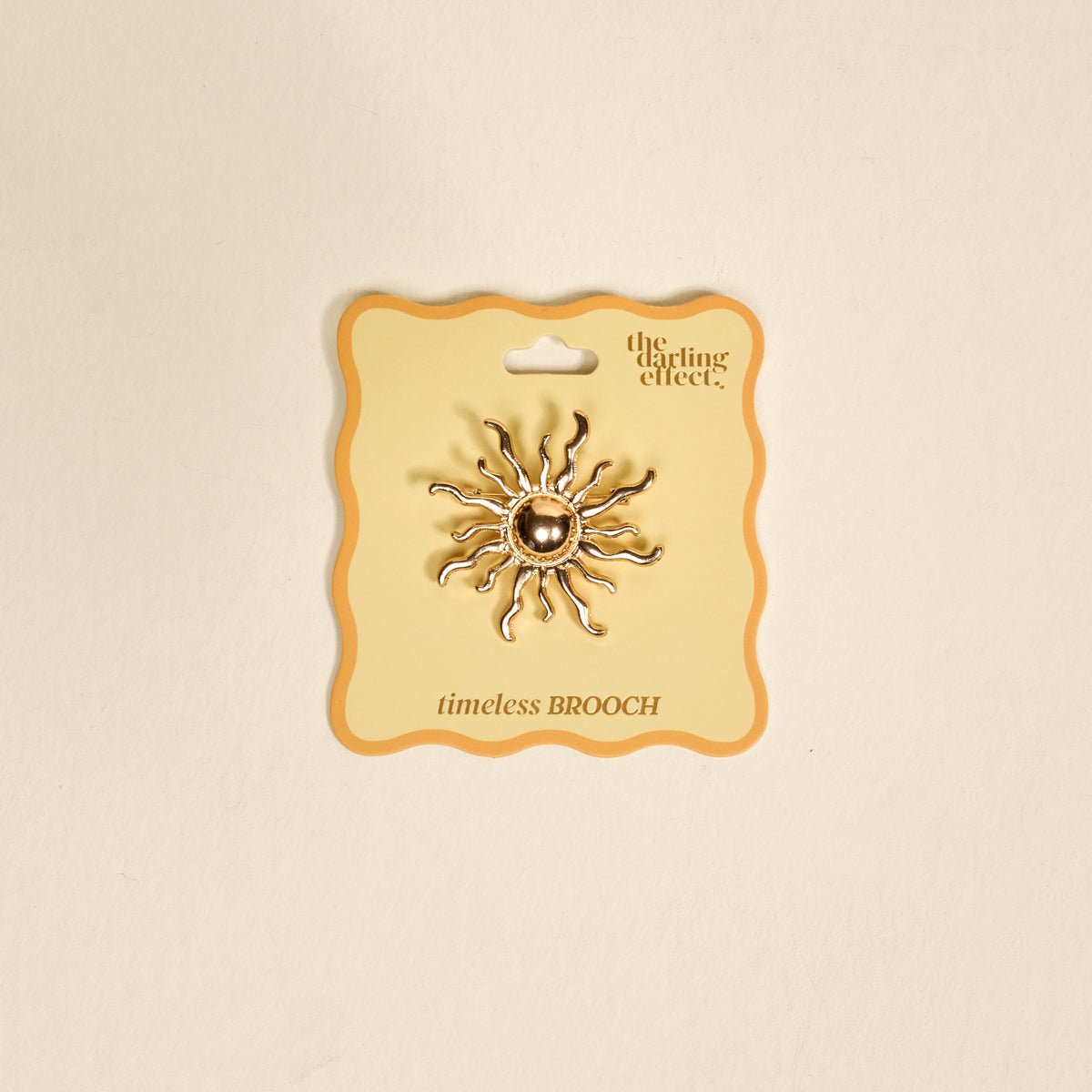 Timeless Brooch, A small gold brooch pin shaped like a teddy bear and covered edge to edge in clear rhinestones, with a gold bow at its neck, shown on a tan background.