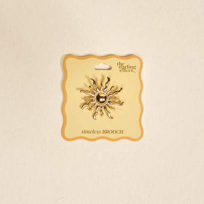 Timeless Brooch, A small gold brooch pin shaped like a teddy bear and covered edge to edge in clear rhinestones, with a gold bow at its neck, shown on a tan background.