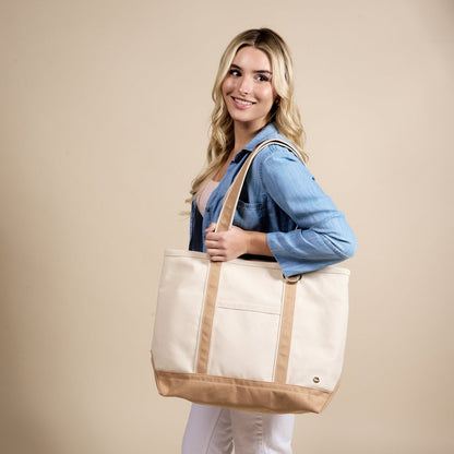 The Signature Canvas Tote Bag, A natural canvas tote bag with black webbing straps, a front pocket, and a gold D-ring, shown against a cream background.