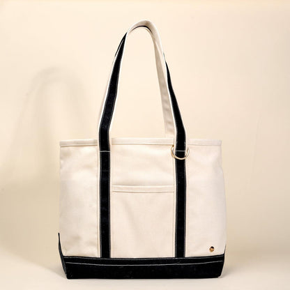The Signature Canvas Tote Bag, A natural canvas tote bag with black webbing straps, a front pocket, and a gold D-ring, shown against a cream background.