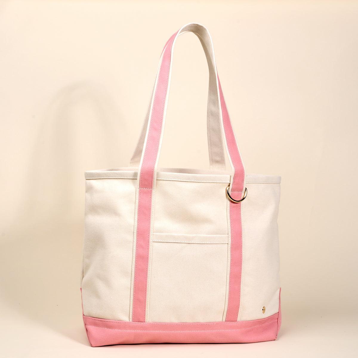 The Signature Canvas Tote Bag, A natural canvas tote bag with black webbing straps, a front pocket, and a gold D-ring, shown against a cream background.