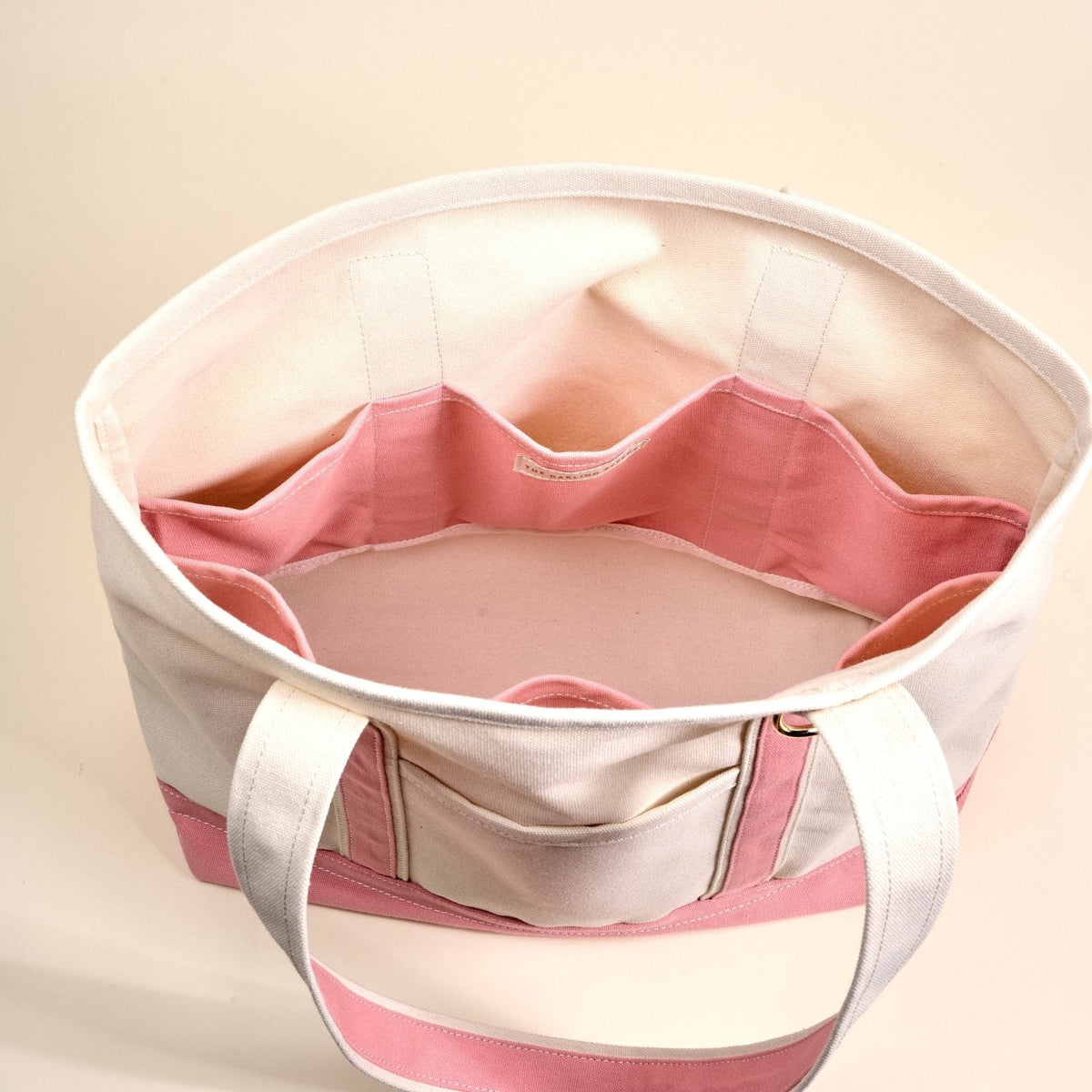 The Signature Canvas Tote Bag, A natural canvas tote bag with black webbing straps, a front pocket, and a gold D-ring, shown against a cream background.