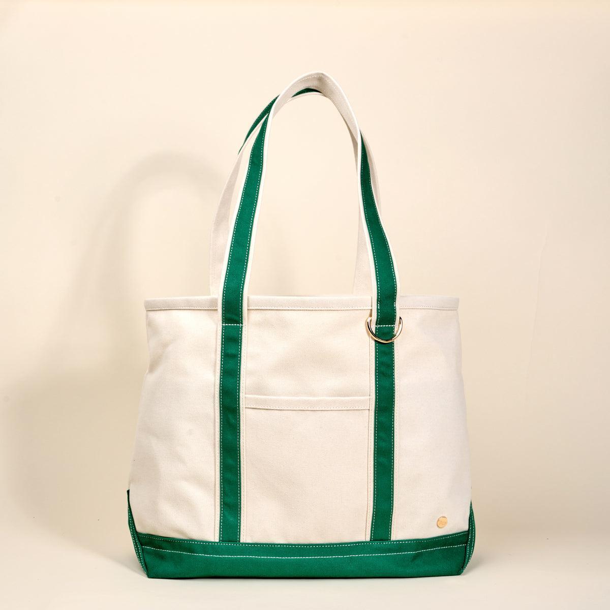 The Signature Canvas Tote Bag, A natural canvas tote bag with black webbing straps, a front pocket, and a gold D-ring, shown against a cream background.