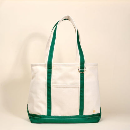 The Signature Canvas Tote Bag, A natural canvas tote bag with black webbing straps, a front pocket, and a gold D-ring, shown against a cream background.