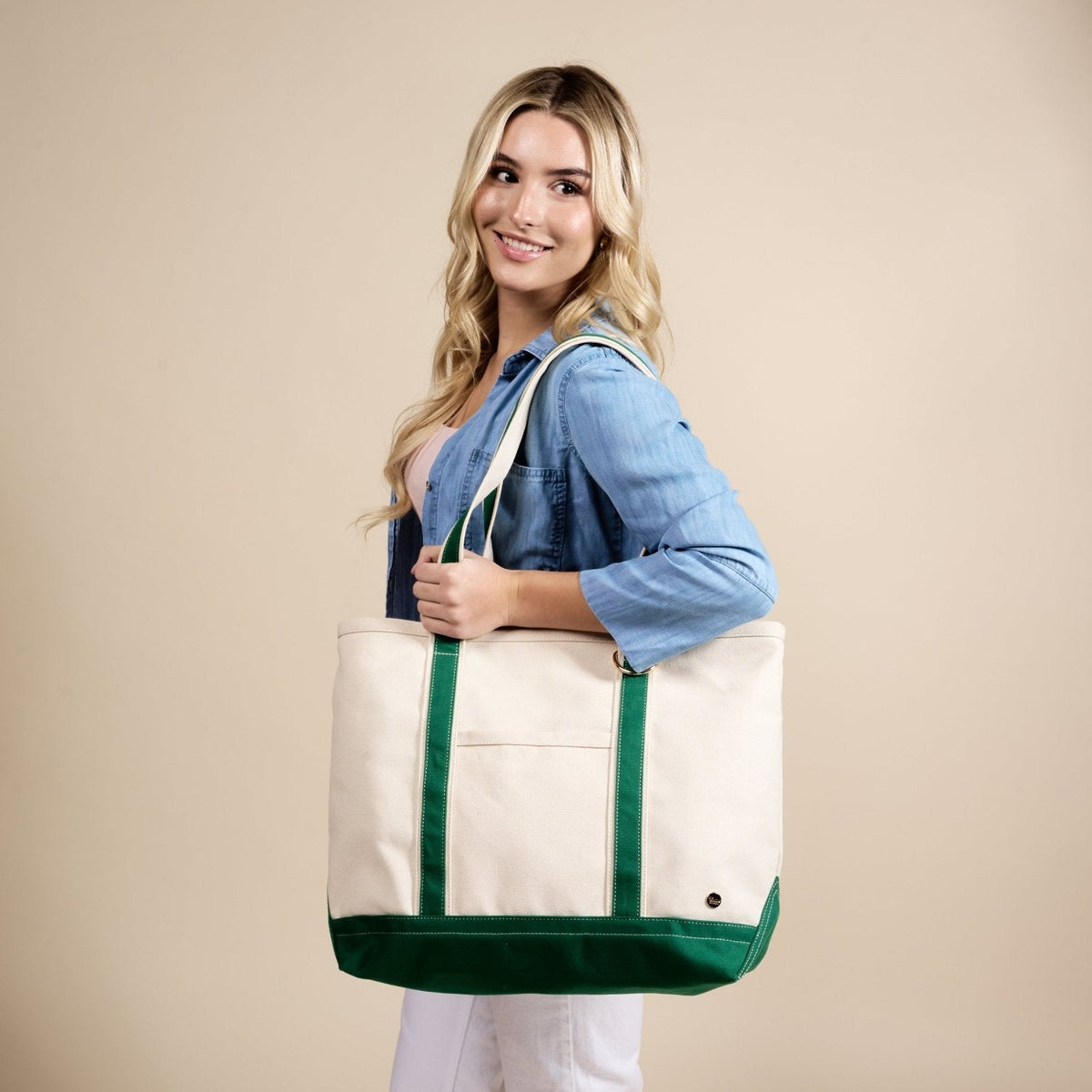 The Signature Canvas Tote Bag, A natural canvas tote bag with black webbing straps, a front pocket, and a gold D-ring, shown against a cream background.