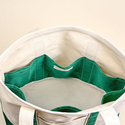 The Signature Canvas Tote Bag, A natural canvas tote bag with black webbing straps, a front pocket, and a gold D-ring, shown against a cream background.