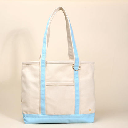 The Signature Canvas Tote Bag, A natural canvas tote bag with black webbing straps, a front pocket, and a gold D-ring, shown against a cream background.